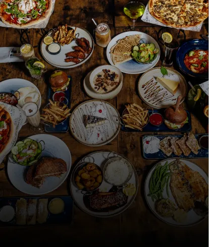 Table with various dishes including pizza, burgers, fries, salads, and desserts on wooden surface.