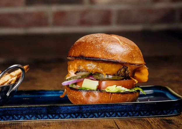 Cheeseburger with lettuce, tomato, pickles, and onions on a bun served on a blue tray with fries.