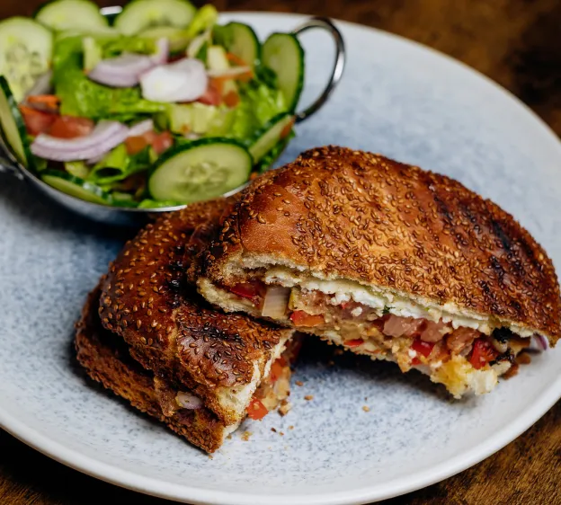 Sesame seed sandwich with mixed vegetable filling and side salad in a bowl on a white plate.