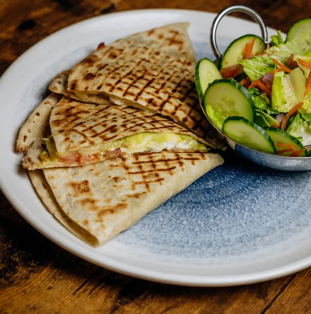 Grilled quesadilla slices with cheese and tomato served with fresh cucumber salad on a white plate.