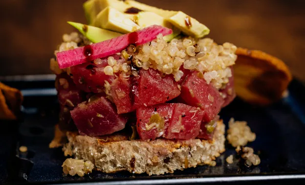 Open sandwich with diced tuna, quinoa, avocado, and beetroot on whole grain bread.