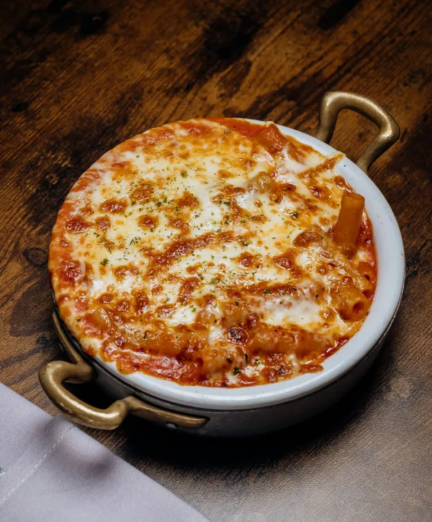 Baked pasta dish with melted cheese in a small round pan on a wooden table.