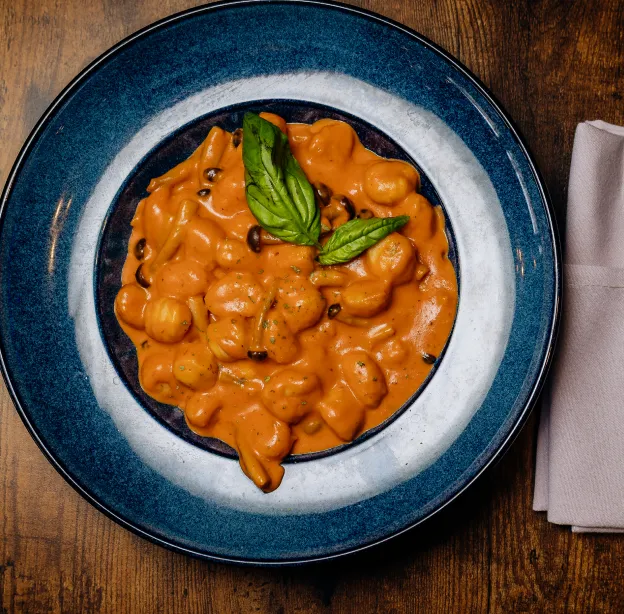 Plate of gnocchi pasta in creamy tomato sauce garnished with fresh basil leaves on wooden table.