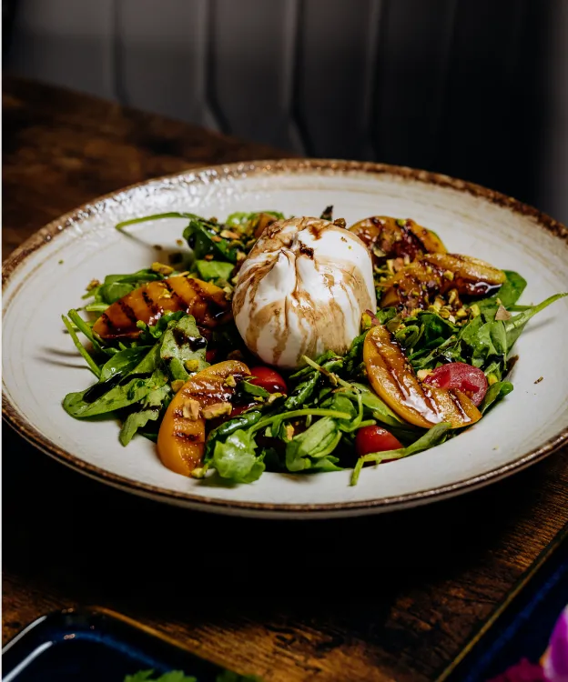 Grilled peach and arugula salad with burrata cheese and balsamic drizzle on a ceramic plate.