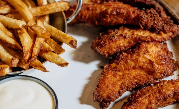 Plate with crispy fried chicken tenders, French fries, and a cup of creamy dipping sauce.