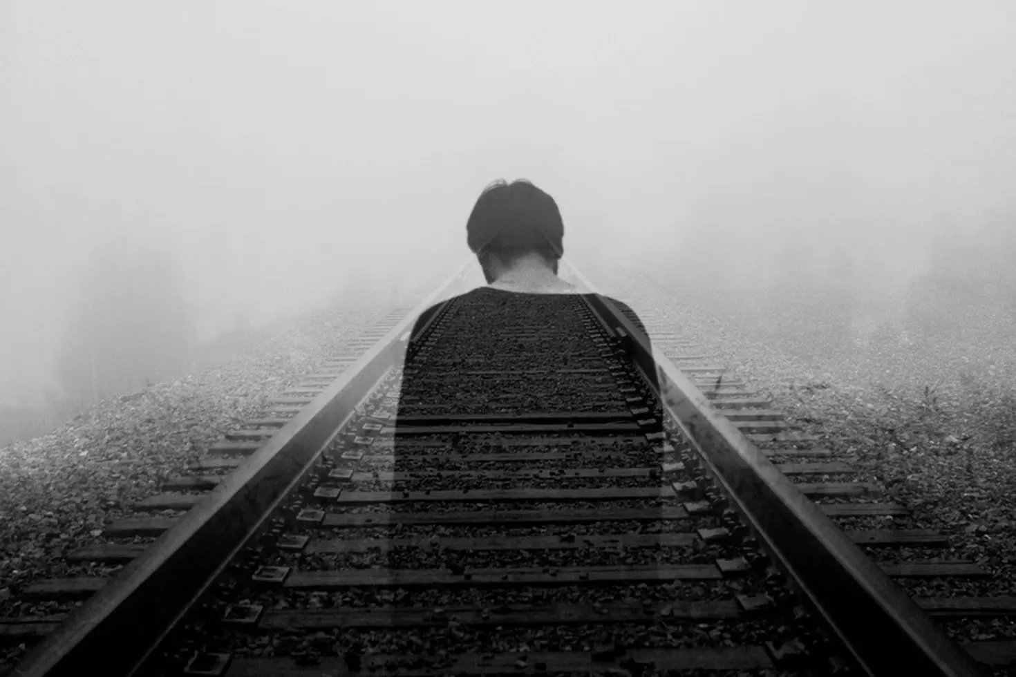 Double exposure of a person with back turned blending into foggy railway tracks.