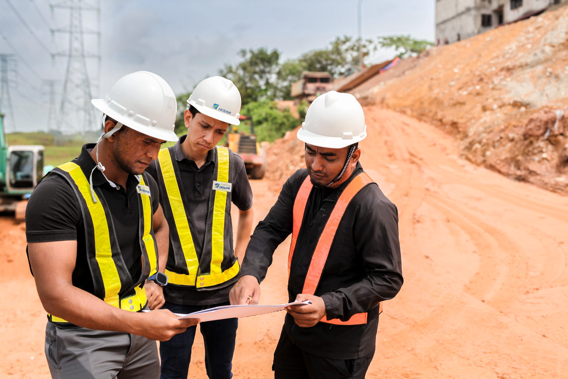 IKRAM engineers in hard hats and hi-vis vests reviewing site drawings on an earthworks cut slope