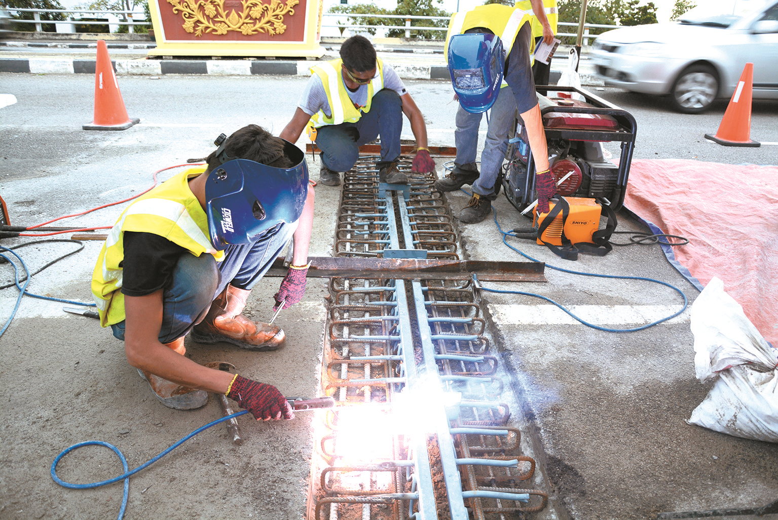 Workers welding a bridge expansion joint into a road surface, with traffic cones closing the lane