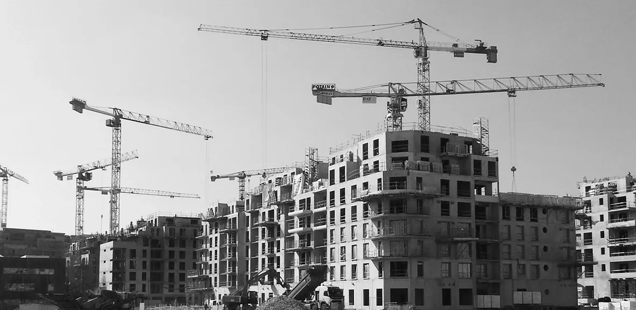 Plusieurs grues autour de plusieurs immeubles en construction dans un chantier urbain.