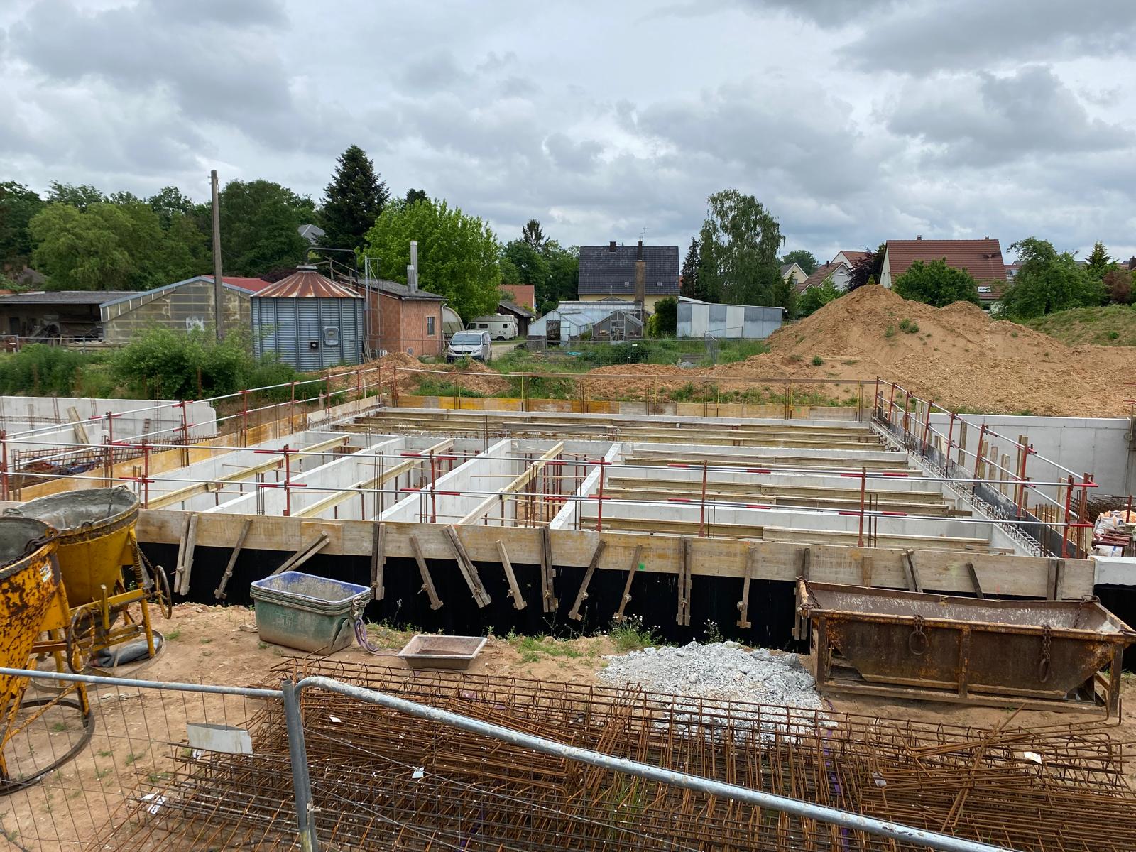 Chantier de construction avec fondations en béton, matériaux et grilles métalliques sur un terrain ouvert.