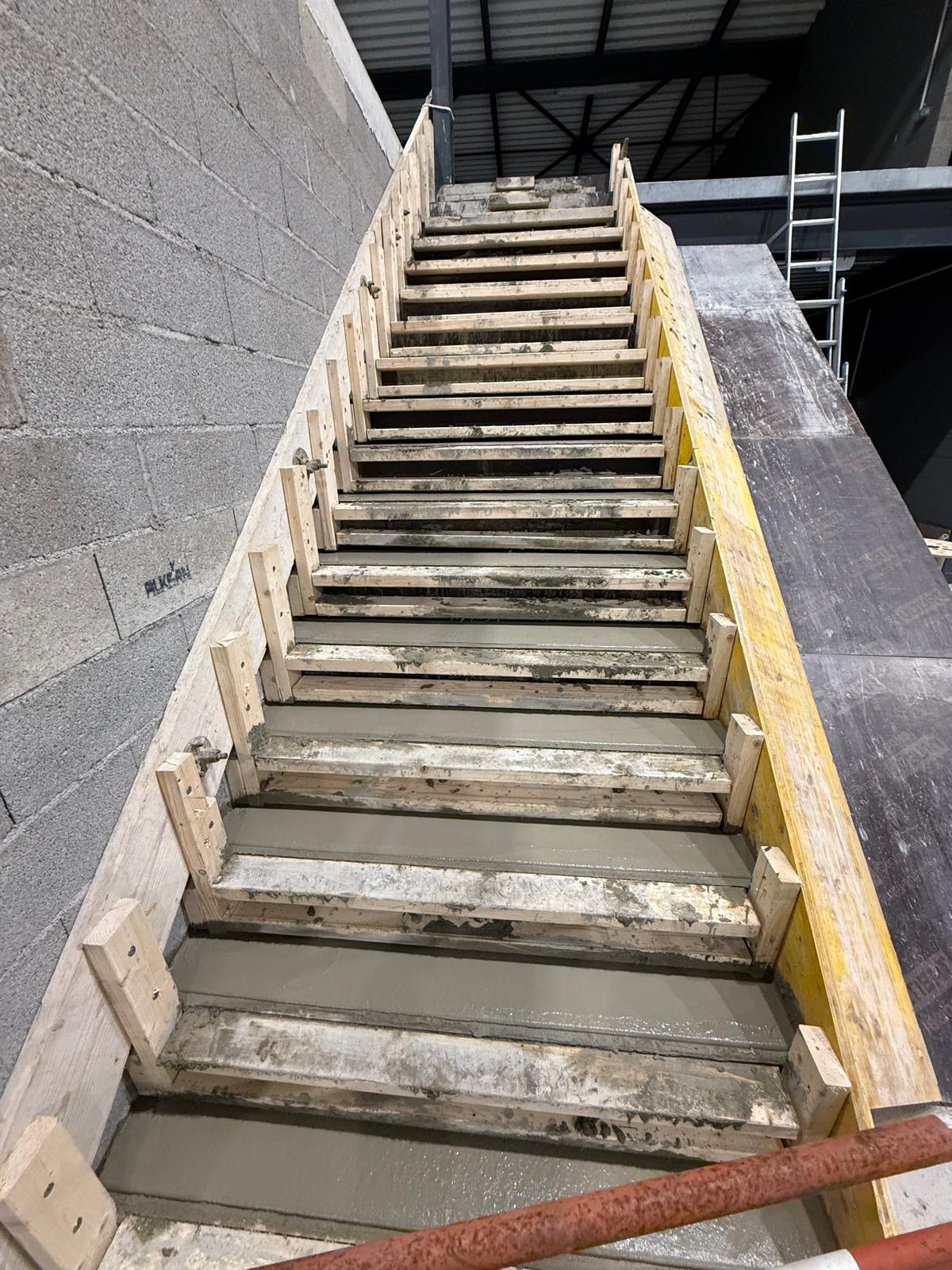 Escalier en construction avec des marches en béton frais dans un coffrage en bois dans un bâtiment industriel.
