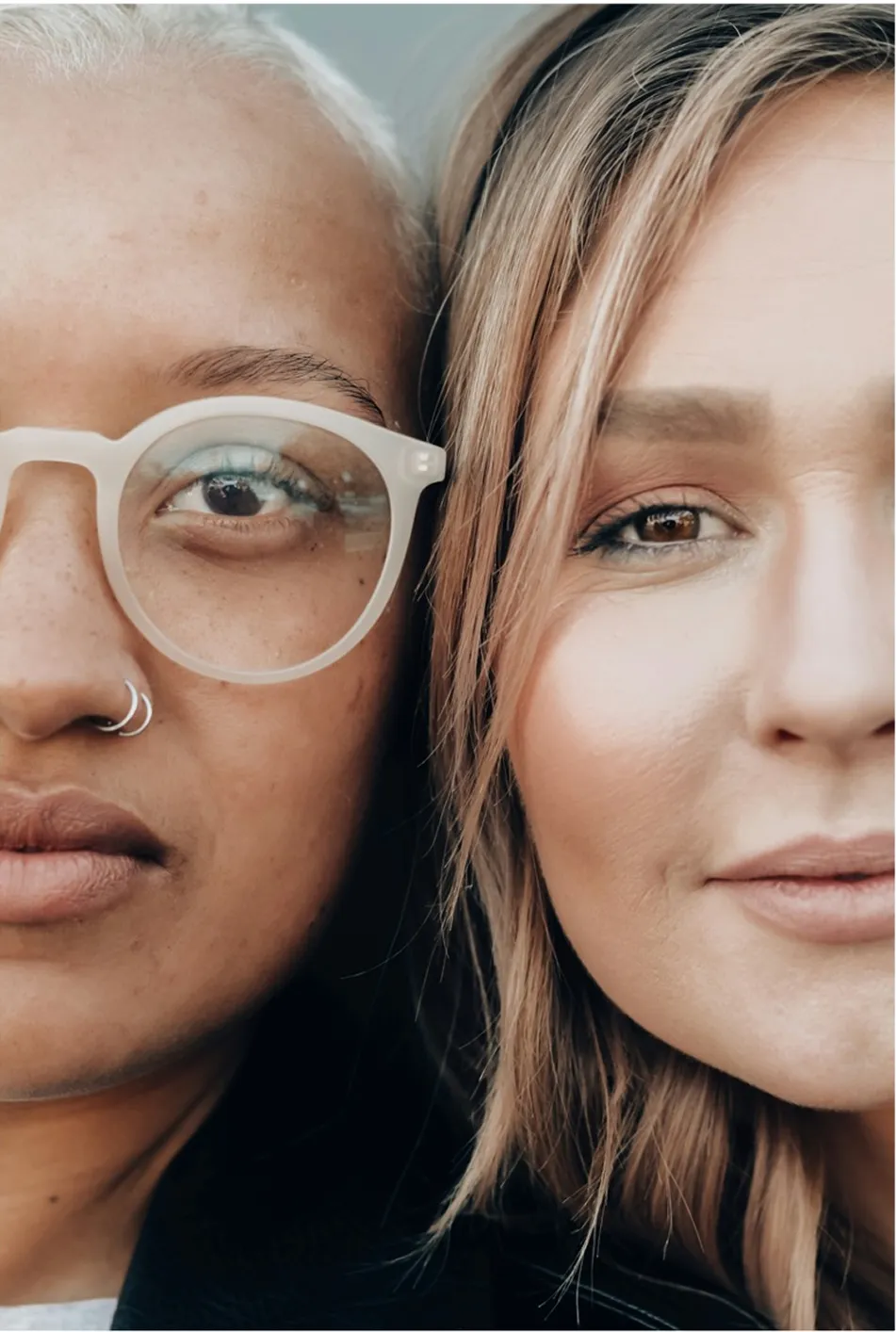 Close-up of two women's faces side by side, one wearing glasses and a nose ring.