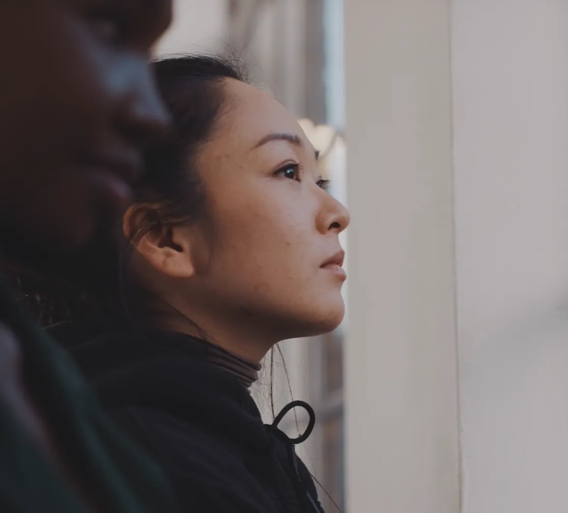Side profile of a woman looking thoughtfully ahead next to a blurred man in the foreground.
