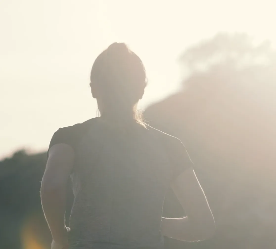 Silhouette of a person jogging outdoors with bright sunlight and trees in the background.