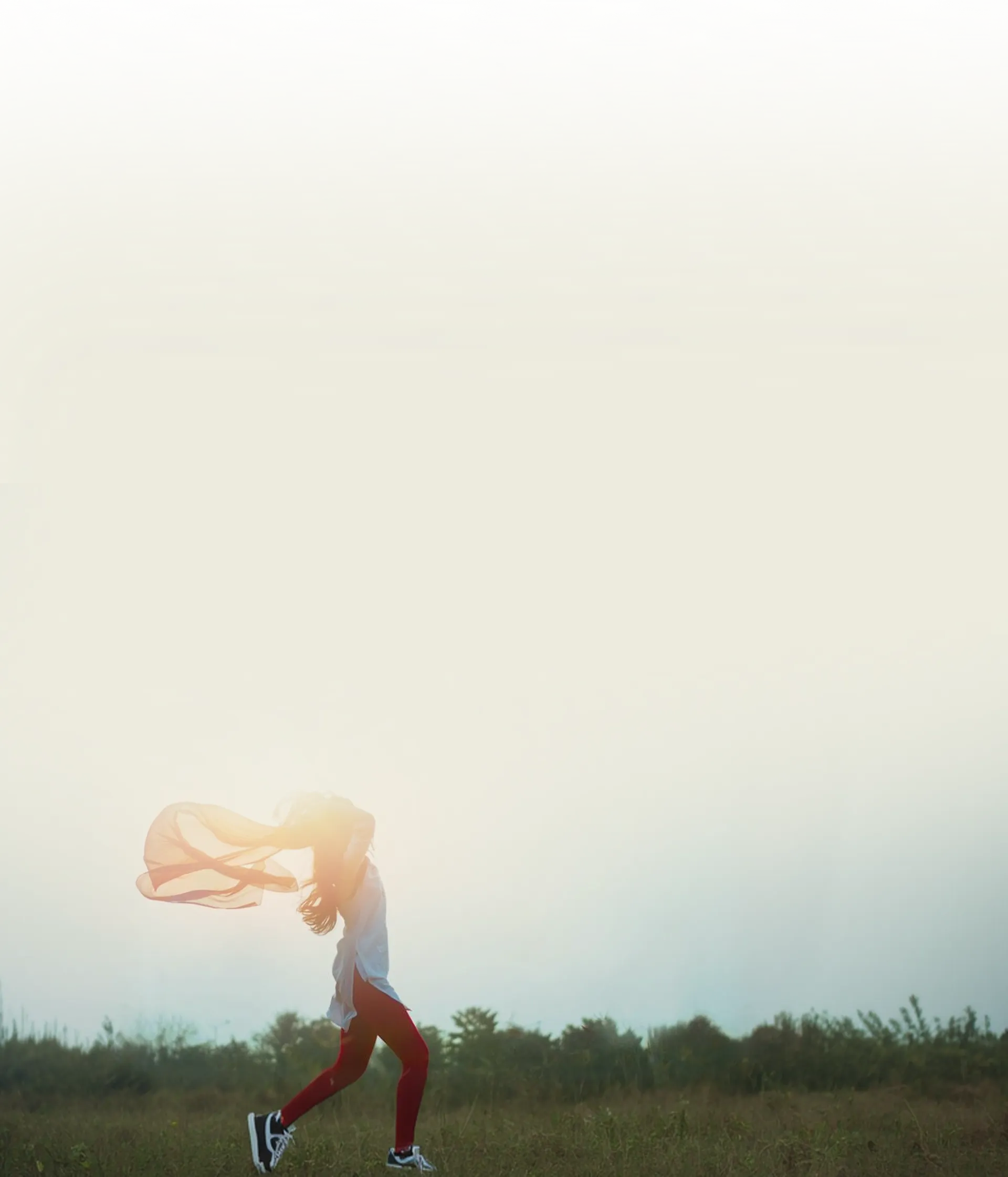 Person running in a field with a flowing scarf in the wind during sunrise or sunset.