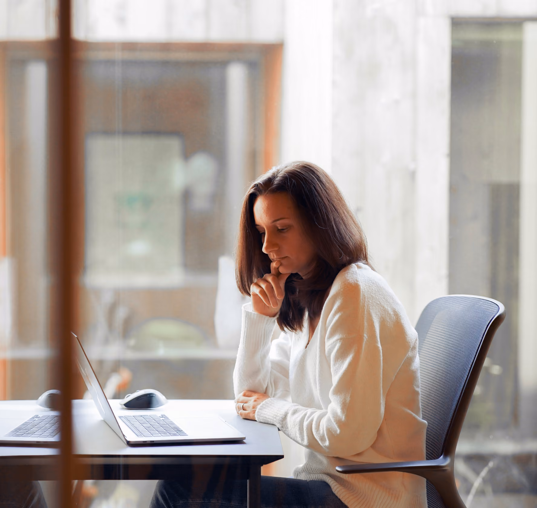 Person thoughtfully reviewing something on a laptop by a window