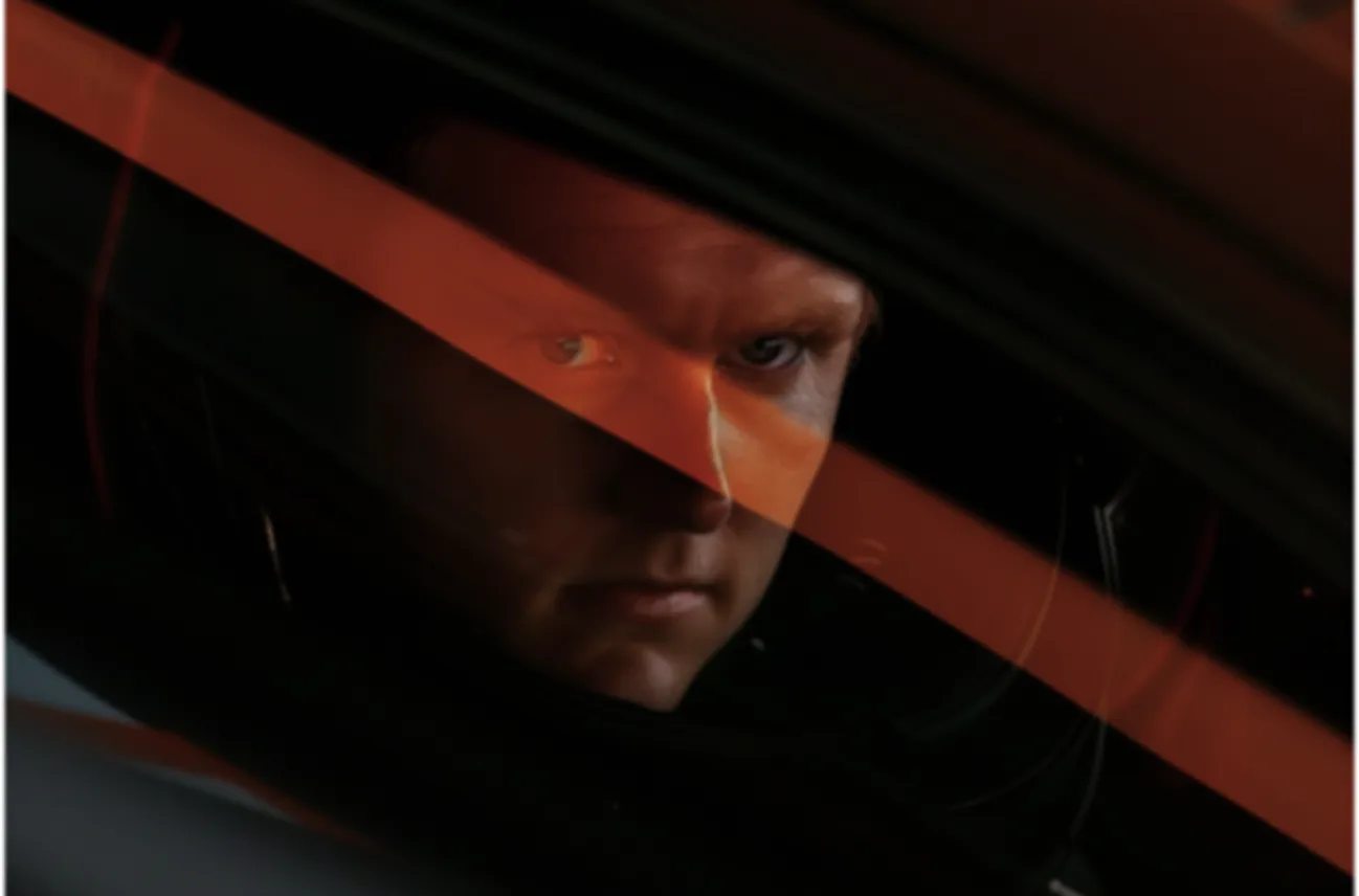 Man with intense expression looking through a car window with orange light streaks.