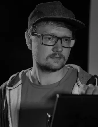 Man wearing glasses and a cap looking intently at a screen or device in front of him.