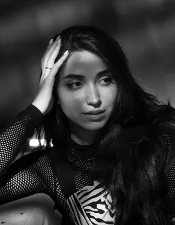 Black and white portrait of a woman with long hair touching her face, looking to the side thoughtfully.
