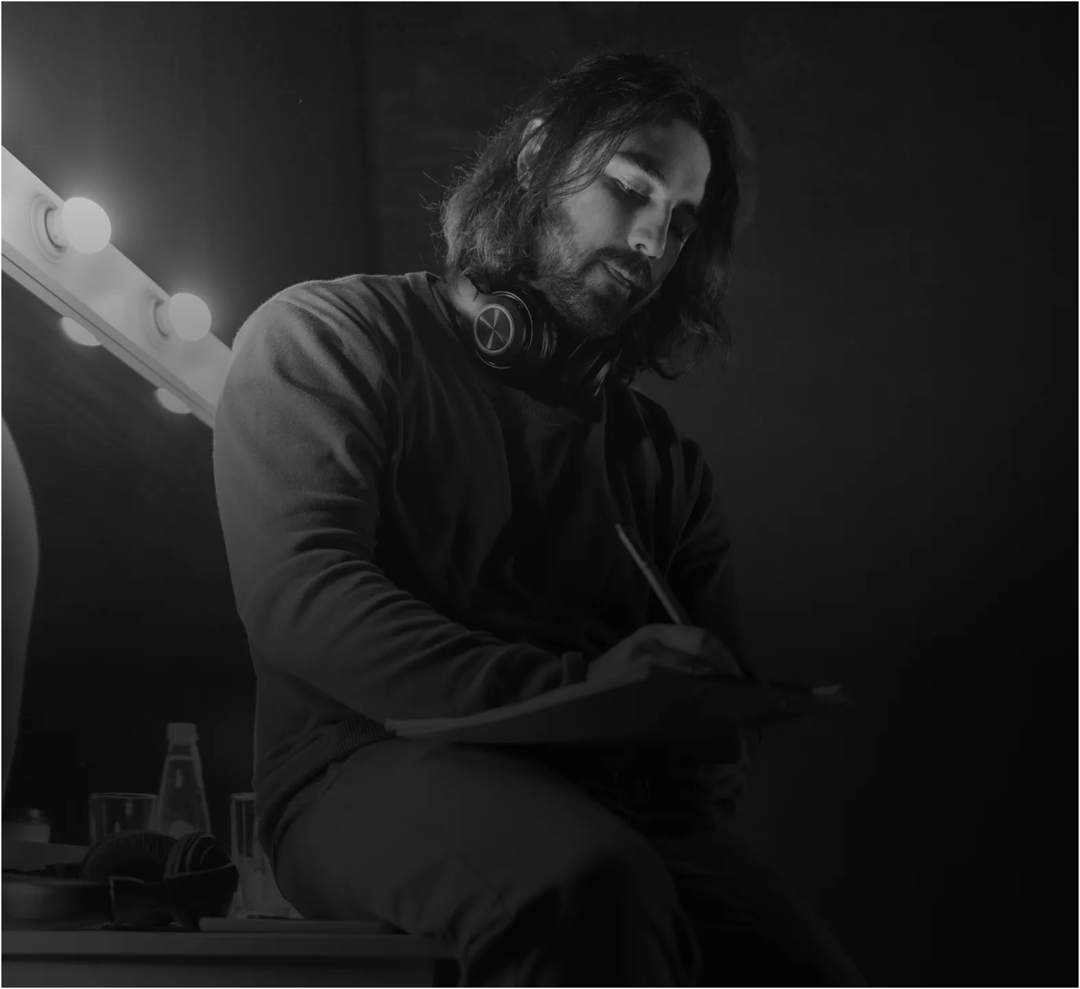 Man with mustache sitting alone in dark theater, smiling, with bright light shining behind him.