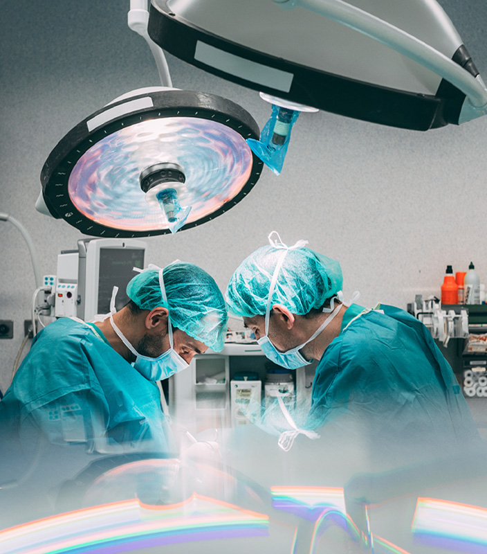 Two surgeons in teal scrubs and masks performing surgery under bright operating room lights.