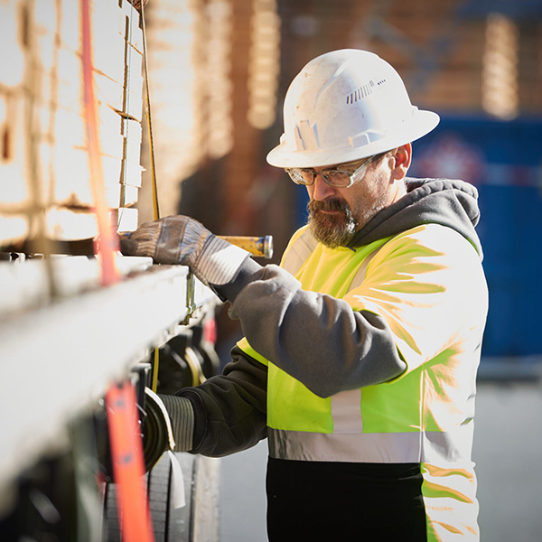 Construction worker in hard hat and gloves adjusting materials on a pallet with a level tool.