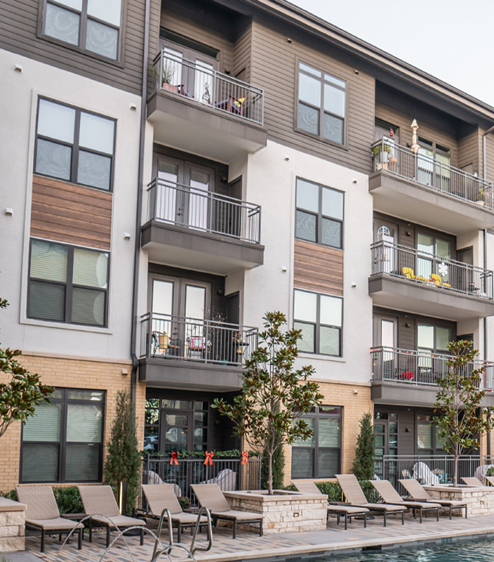 Modern apartment building with balconies and lounge chairs around a swimming pool.