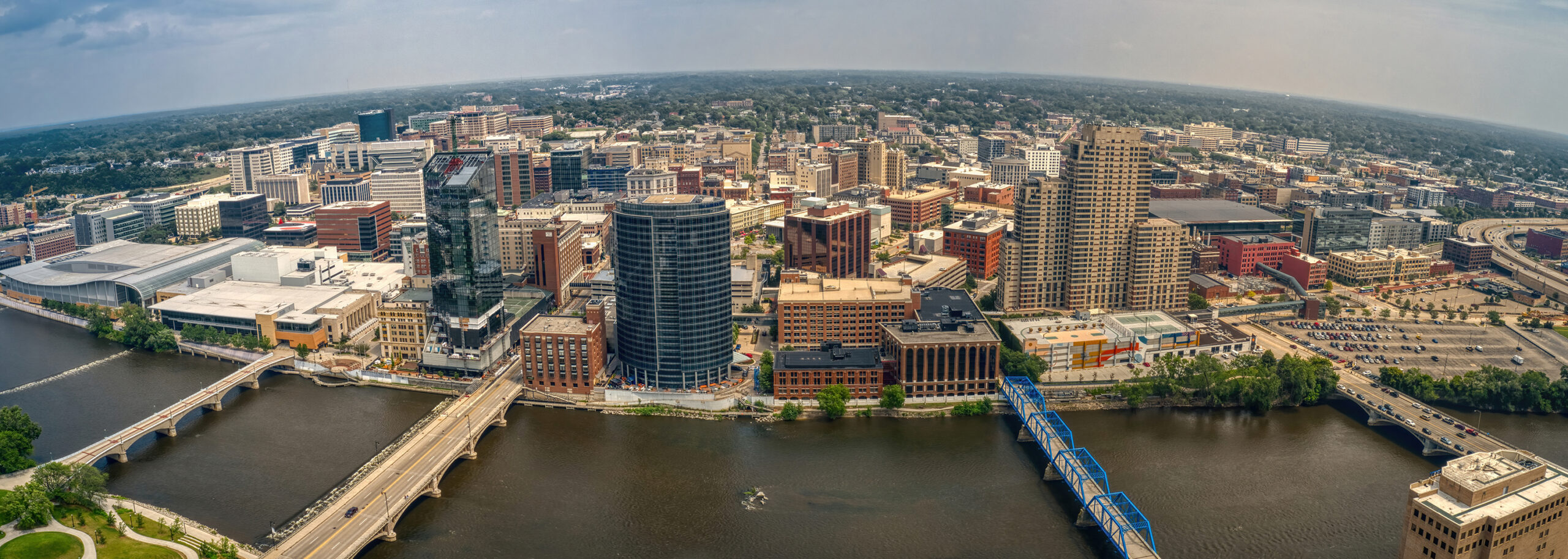 Aerial view of a Grand Rapids, MI skyline with multiple bridges crossing a river under a cloudy sky.