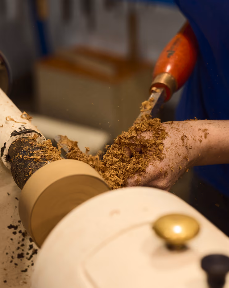 Close-up of hand shaping wood on a lathe with a chisel, wood shavings flying around.