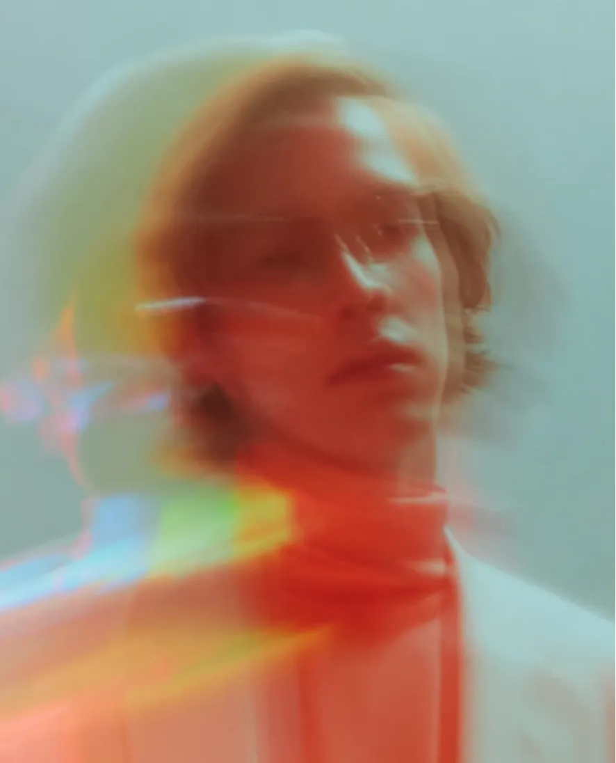 Blurred portrait of a person with reddish tones and light streaks on a pale background.