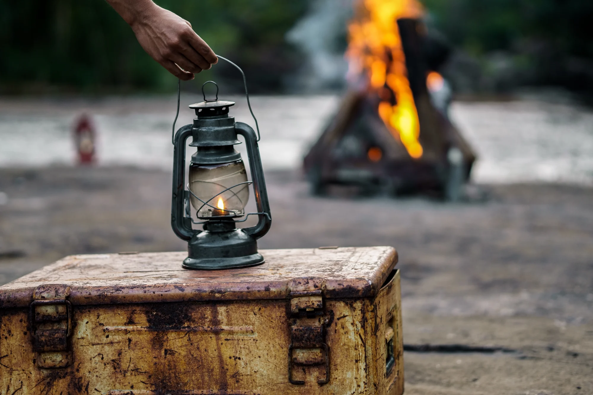 A lantern being placed beside a riverside fire for sundowners
