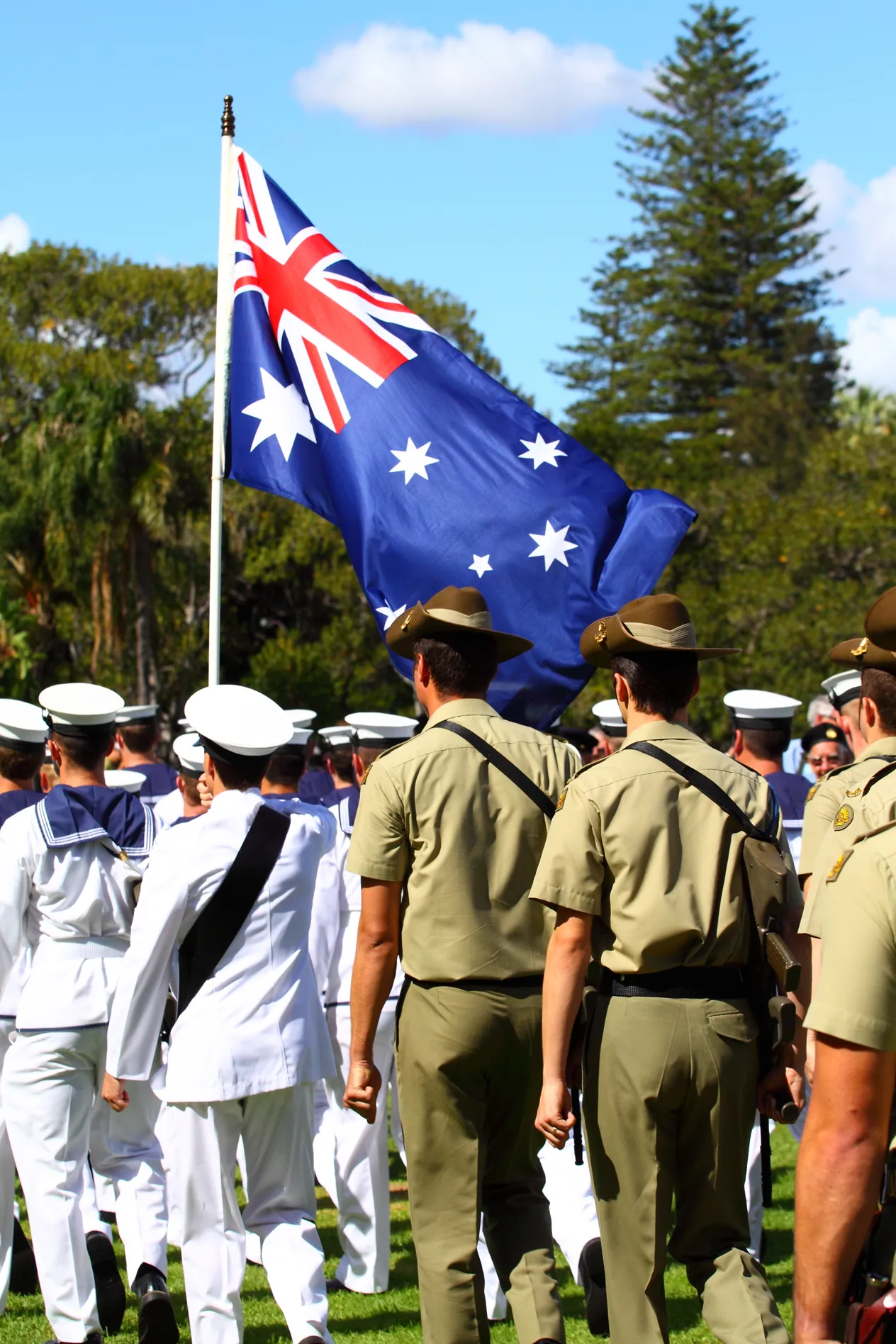 Uniformed Australian military personnel marching outdoors, carrying the Australian flag.