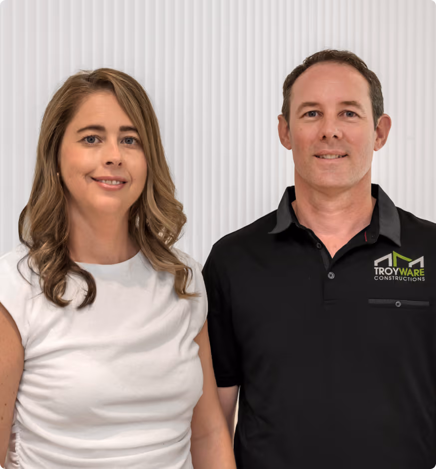 Man and woman standing side by side, smiling; man wears Troyware Constructions black polo shirt.