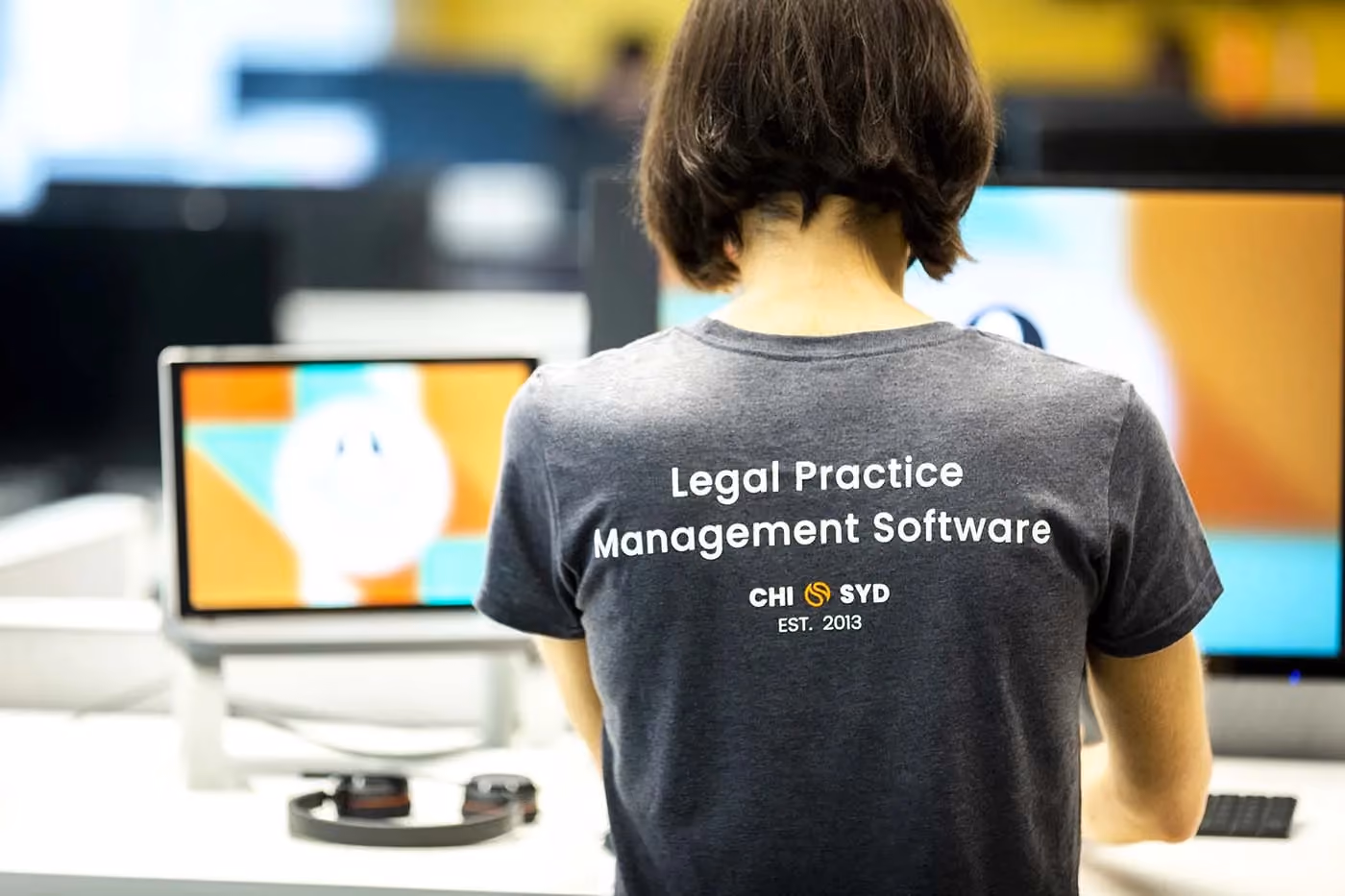 Person wearing a t-shirt that reads Legal Practice Management Software, sitting in front of computer screens.