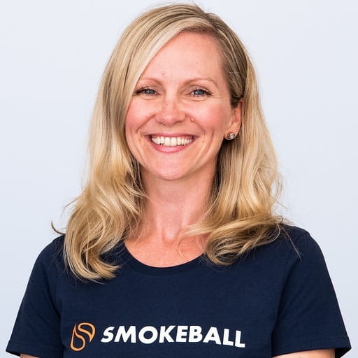 Smiling woman with blonde hair wearing a navy blue Smokeball t-shirt against a light background.