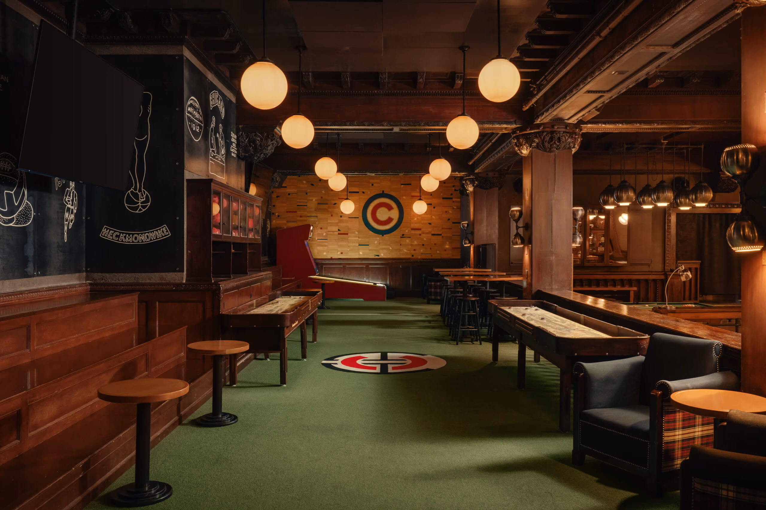 Cozy game room with shuffleboard tables, arcade machine, round hanging lights, and wood-paneled walls.