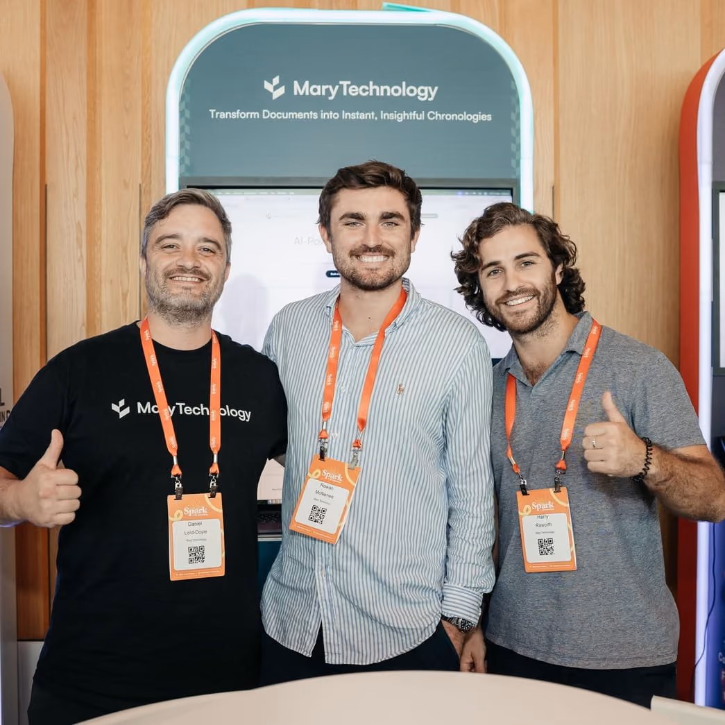 Three men smiling wearing conference badges and standing in front of a Mary Technology booth.