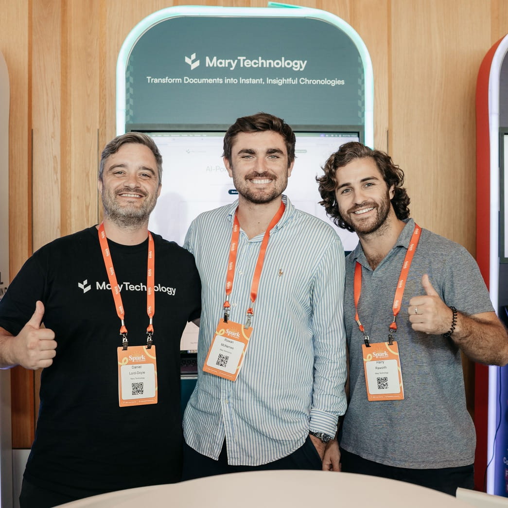 Three men smiling wearing conference badges and standing in front of a Mary Technology booth.
