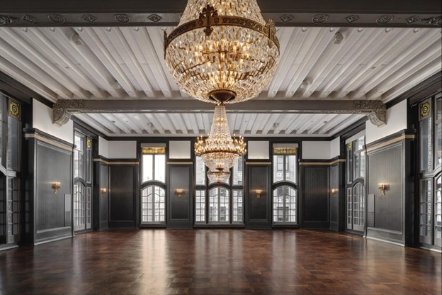 Elegant empty ballroom with dark walls, large windows, wooden floor, and three crystal chandeliers.