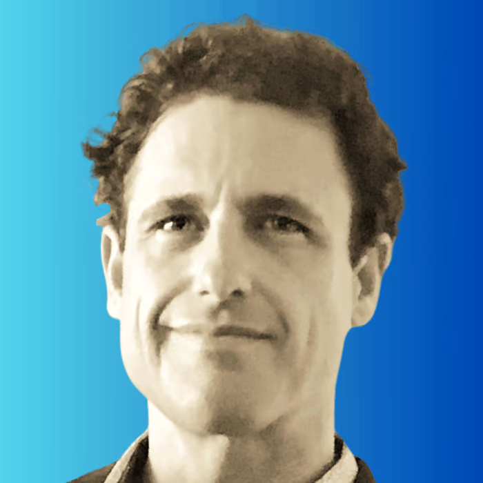 Headshot of a middle-aged man with short curly hair smiling against a blue gradient background.