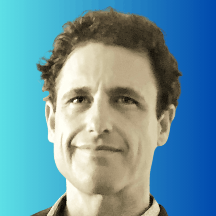 Headshot of a middle-aged man with short curly hair smiling against a blue gradient background.