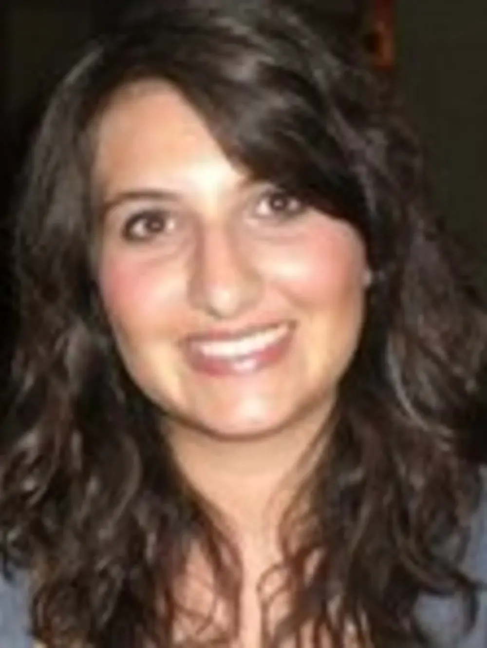 Smiling woman with long curly dark hair against a dark background.