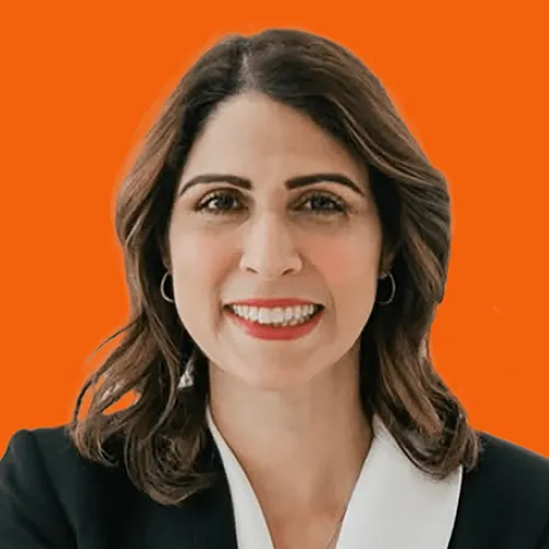 Smiling woman with shoulder-length brown hair wearing a black blazer and white blouse on an orange background.