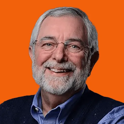 Smiling older man with gray hair, beard, glasses, wearing a blue shirt and dark vest on orange background.