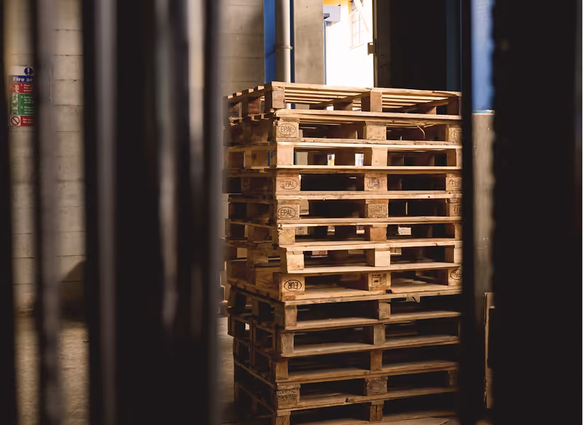 Stacked wooden Euro pallets in a storage room with concrete walls, viewed through dark frames in the foreground