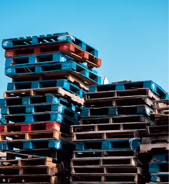 Several stacked wooden and plastic shipping pallets against a clear blue sky
