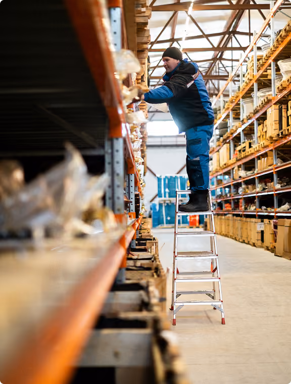 Warehouse worker picking goods from a ladder in high-bay racking