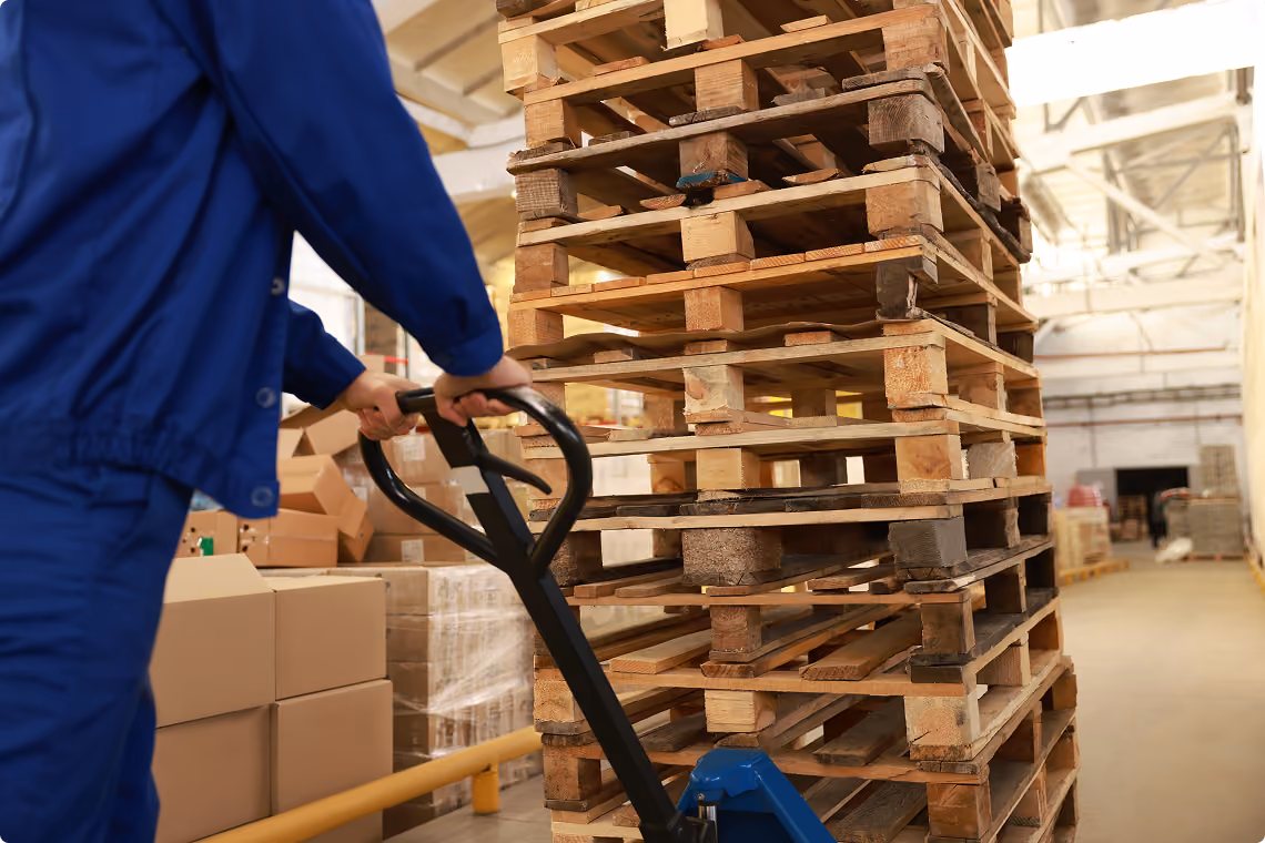 Worker with a pallet truck beside stacked Euro pallets in a warehouse