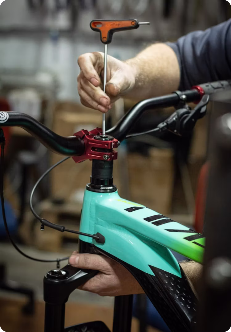Hand using a T-handle wrench to adjust the handlebar stem on a turquoise mountain bike.