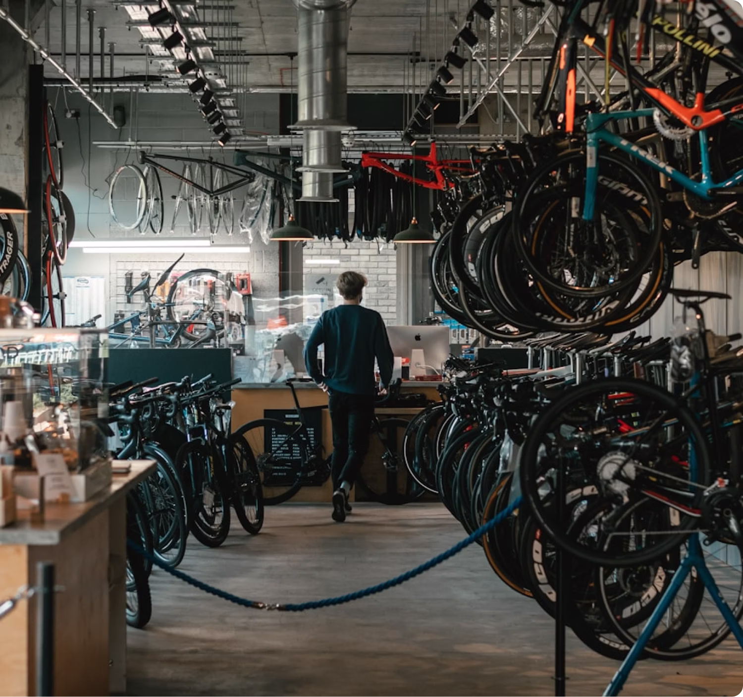 Person walking toward counter in a bike shop with bikes and wheels displayed all around.